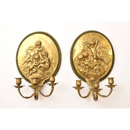 574 - A pair of reproduction cast brass candle sconces Of oval form and cast with opposing scenes of putti... 