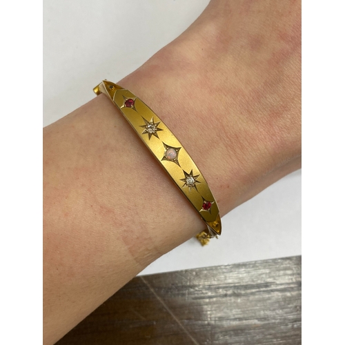 28 - An opal, diamond and red paste bangle, designed as a central round cabochon opal flanked to each sid... 