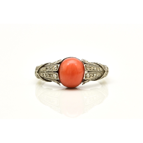 38 - A French Art Deco coral and diamond ring, designed as a single oval cabochon coral mounted within gr... 