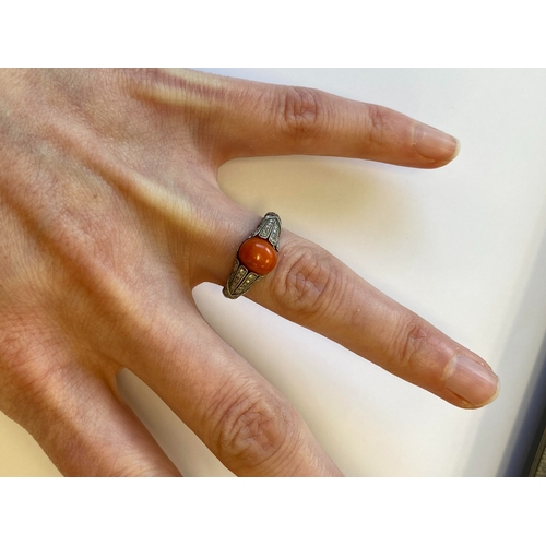 38 - A French Art Deco coral and diamond ring, designed as a single oval cabochon coral mounted within gr... 