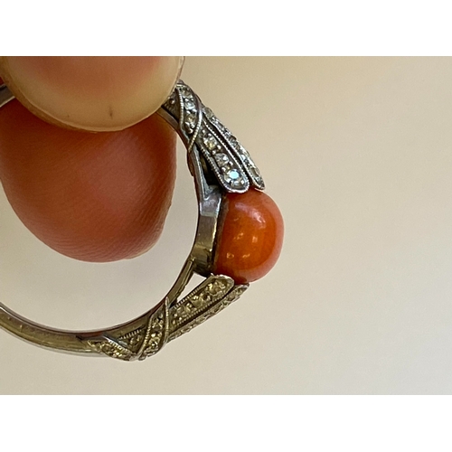 38 - A French Art Deco coral and diamond ring, designed as a single oval cabochon coral mounted within gr... 