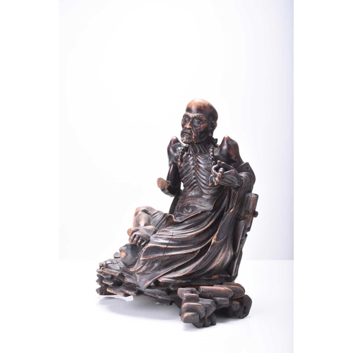 114 - A Chinese carved wood figure of a seated Luohan, Qing Dynasty The emaciated figure sitting on a rock... 