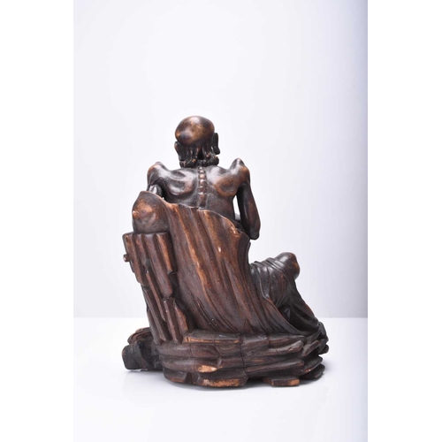 114 - A Chinese carved wood figure of a seated Luohan, Qing Dynasty The emaciated figure sitting on a rock... 