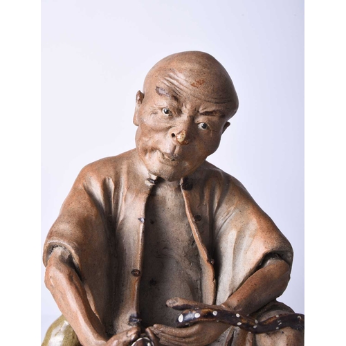 87 - A Chinese Shiwan figure of a seated man, Qing Dynasty Modelled wearing rustic garb and holding a sna... 