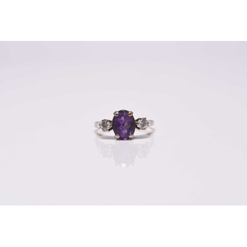 366 - A three stone amethyst and diamond ring, designed as a central oval mixed cut amethyst claw set in w... 