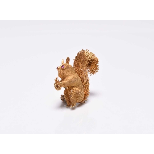 379 - A yellow metal squirrel brooch, naturalistically modelled with faceted ruby set eyes and holding a p... 