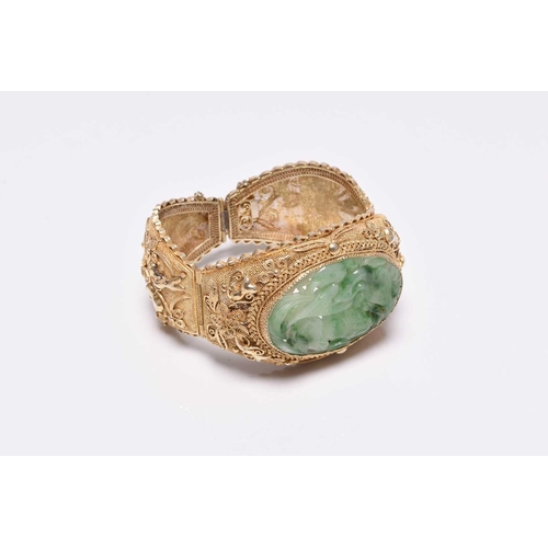 392 - A jade and gilt metal bangle, designed as a central carved jade plaque depicting a bird amongst frui... 