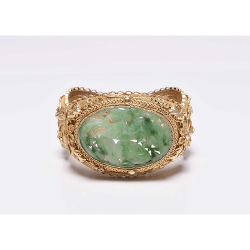 392 - A jade and gilt metal bangle, designed as a central carved jade plaque depicting a bird amongst frui... 