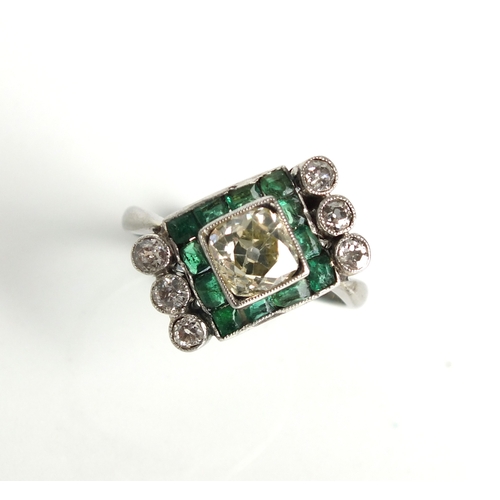 51 - An Art Deco diamond and emerald ring, designed as a central old mine cut diamond box set in white me... 