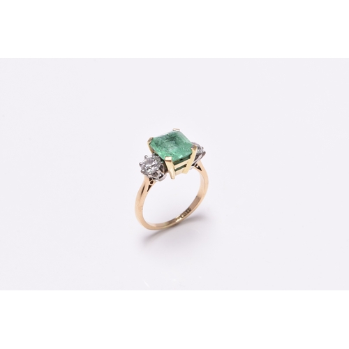 56 - A three stone emerald and diamond ring, designed as a central square faceted emerald claw set in yel... 