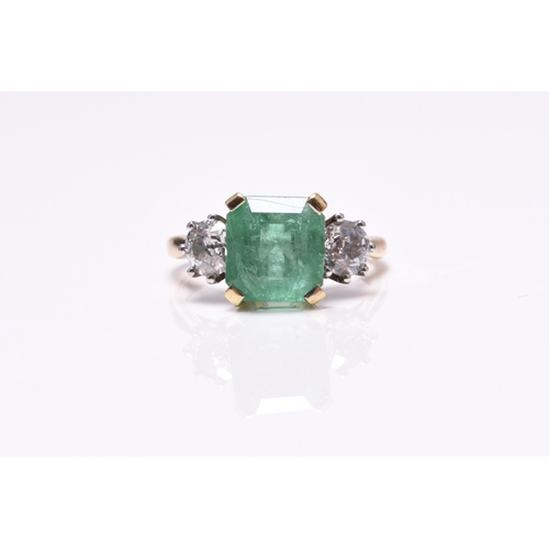 56 - A three stone emerald and diamond ring, designed as a central square faceted emerald claw set in yel... 