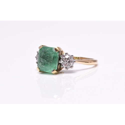 56 - A three stone emerald and diamond ring, designed as a central square faceted emerald claw set in yel... 