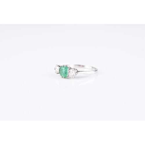 121 - A graduated three stone emerald and diamond ring, designed as a central trap cut emerald flanked to ... 