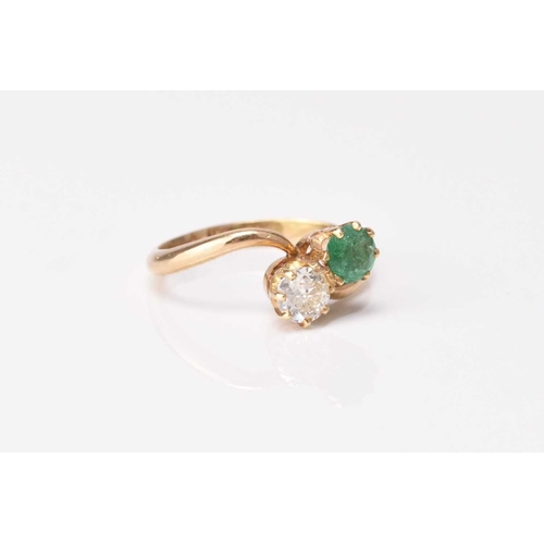 130 - A two stone emerald and diamond crossover ring, the brilliant cut diamond and round mixed cut emeral... 