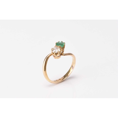 130 - A two stone emerald and diamond crossover ring, the brilliant cut diamond and round mixed cut emeral... 