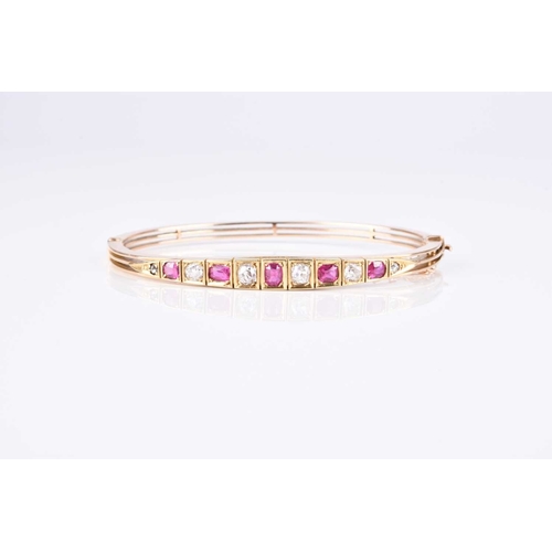 132 - An early 20th century diamond and ruby set hinged bangle, designed as five graduated oval mixed cut ... 