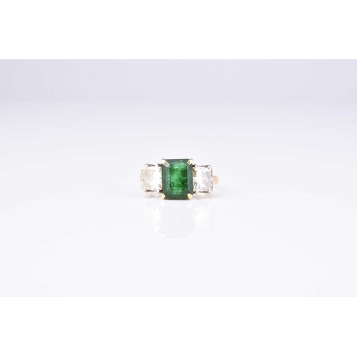 149 - An 18ct gold three stone emerald and diamond ring, designed as a central trap cut emerald claw set i... 