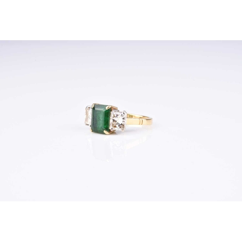 149 - An 18ct gold three stone emerald and diamond ring, designed as a central trap cut emerald claw set i... 