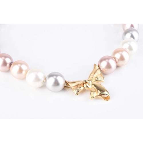 65 - A large simulated pearl necklace, with yellow metal stylised ribbon clasp, 43cm long, the clasp indi... 