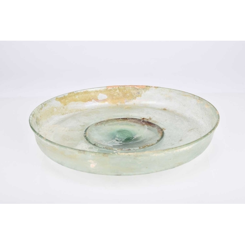 35 - A Roman pale green glass footed dish Jordan, 2nd-3rd century AD The shallow bowl with straight sligh... 