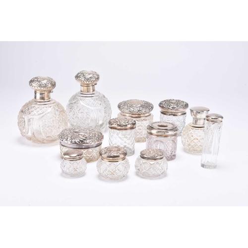 60 - A group of twelve silver topped glass dressing table jars/bottles, most silver mounts with embossed ... 