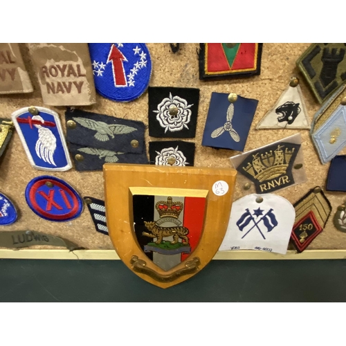 394 - A BOARD WITH NUMEROUS MILITARY CLOTH BADGES AND A MILITARY PLAQUE