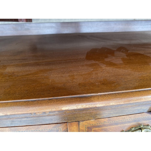 2140 - AN INLAID MAHOGANY BOW FRONT SIDEBOARD WITH TWO DOORS AND TWO DRAWERS - LEG REQUIRES REPAIR