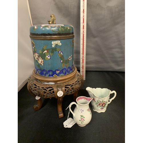 773 - A LARGE ORIENTAL CLOISONNE LIDDED JAR ON AN ORNATE CARVED WOODEN STAND AND TWO SMALL JUGS