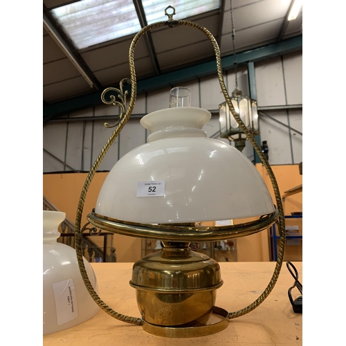 52 - A DECORATIVE BRASS OIL LAMP WITH AN OPAQUE GLASS SHADE AND HANGING HANDLE.  TO INCLUDE A SPARE SHADE