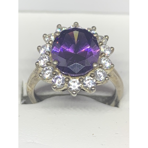 524 - A SILVER RING MARKED 925 WITH A LARGE CENTRE PURPLE STONE SURROUNDED BY FOURTEEN CLEAR STONES IN A P... 