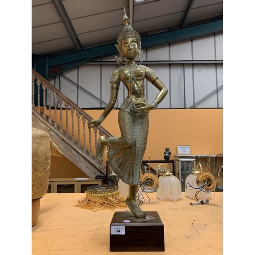 34 - A LARGE BRASS STATUE OF A ORIENTAL TEMPLE DANCER ON A WOODEN PLINTH - HEIGHT 79 CM