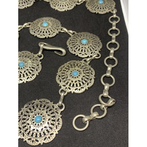 510 - A WHITE METAL BELT WITH ORNATE DISCS AND TURQUOISE STONES IN A NAVAJO STYLE