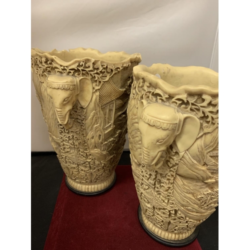 748 - A PAIR OF LARGE ORNATE HEAVILY CARVED IVORINE VASES WITH ELEPHANT HEAD HANDLES (ONE HANDLE A/F)