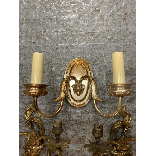 231 - A PAIR OF ORNATE METAL GILT TWIN WALL LIGHTS AND A SINGLE METAL TWIN WALL LIGHT WITH LION'S HEAD DEC... 