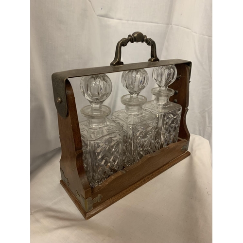 8 - AN OAK AND WHITE METAL TANTALUS WITH THREE DECANTERS