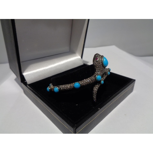 609 - A GOLD AND WHITE GOLD SNAKE BANGLE ENCRUSTED WITH DIAMONDS, RUBY EYES AND BLUE NAJAVO STONES