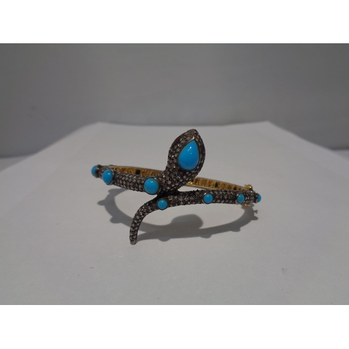 609 - A GOLD AND WHITE GOLD SNAKE BANGLE ENCRUSTED WITH DIAMONDS, RUBY EYES AND BLUE NAJAVO STONES