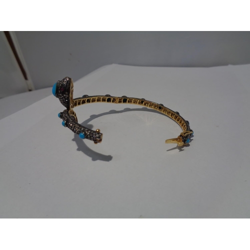 609 - A GOLD AND WHITE GOLD SNAKE BANGLE ENCRUSTED WITH DIAMONDS, RUBY EYES AND BLUE NAJAVO STONES