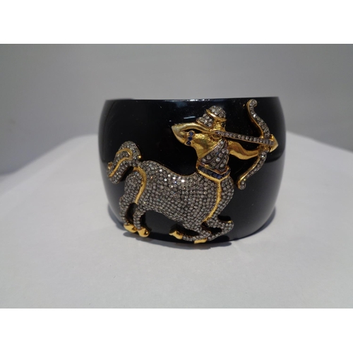 611 - A HEAVY BLACK BANGLE WITH A GOLD AND DIAMOND DECORATION IN THE FORM OF SAGITTARIUS