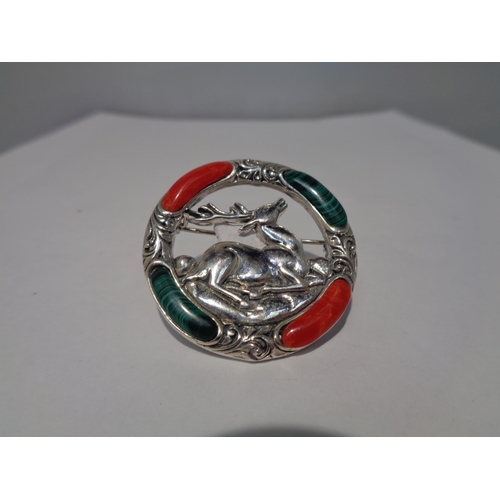 635 - A MARKED SILVER BROOCH WITH RED AND GREEN STONES SURROUNDING A CENTRAL STAG DESIGN