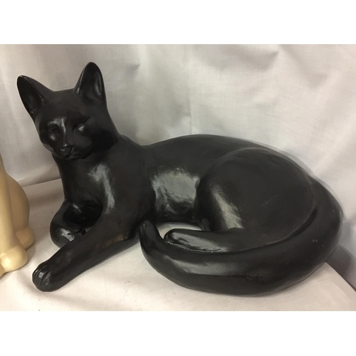 62 - TWO LARGE CAT FIGURES, ONE BLACK, LYING DOWN, LENGTH 36CM, AND A CREAM , HEIGHT 30CM