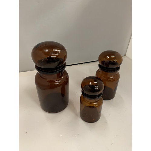 131 - A SET OF THREE GRADUATING BROWN LIDDED GLASS JARS