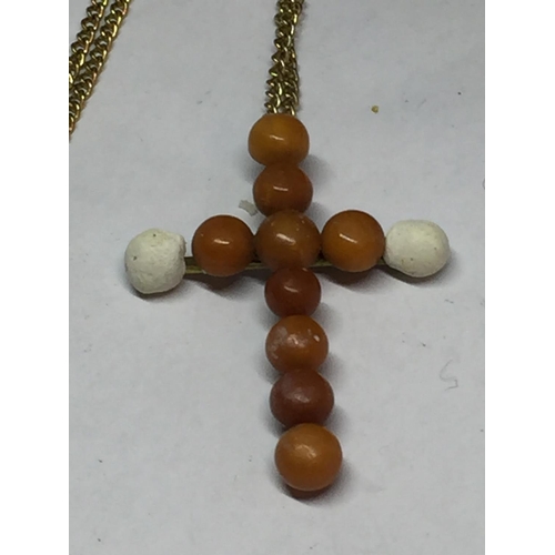 664 - A POSSIBLY BUTTERSCOTCH AMBER CROSS WITH A YELLOW METAL CHAIN