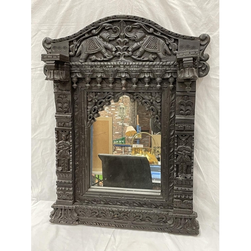 18 - A HEAVILY CARVED EBONY ASIAN STYLE MIRROR WITH ELEPHANT DETAIL 52CM X 79CM