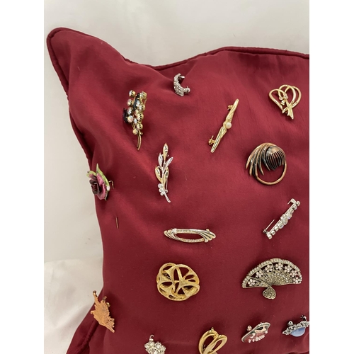 169 - A QUANTITY OF COSTUME JEWELLERY BROOCHES ON A RED CUSHION