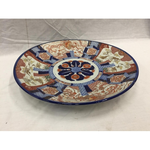 21 - A LARGE IMARI CHARGER WITH HAND PAINTED PANELS RED AND BLUE PATTERNS AND STORKS TO THE RIM, DIAMETER... 