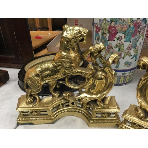 25 - A PAIR OF HEAVY BRASS FIRE DOGS WITH TIGER DECORATION AND A MATCHING BRASS FIRE FENDER