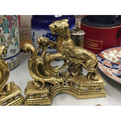 25 - A PAIR OF HEAVY BRASS FIRE DOGS WITH TIGER DECORATION AND A MATCHING BRASS FIRE FENDER