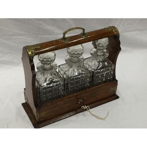 23 - A VINTAGE MAHOGANY TANTALUS DECANTER SET WITH BRASS DETAILING AND A KEY