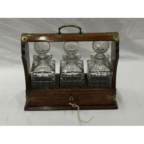 23 - A VINTAGE MAHOGANY TANTALUS DECANTER SET WITH BRASS DETAILING AND A KEY